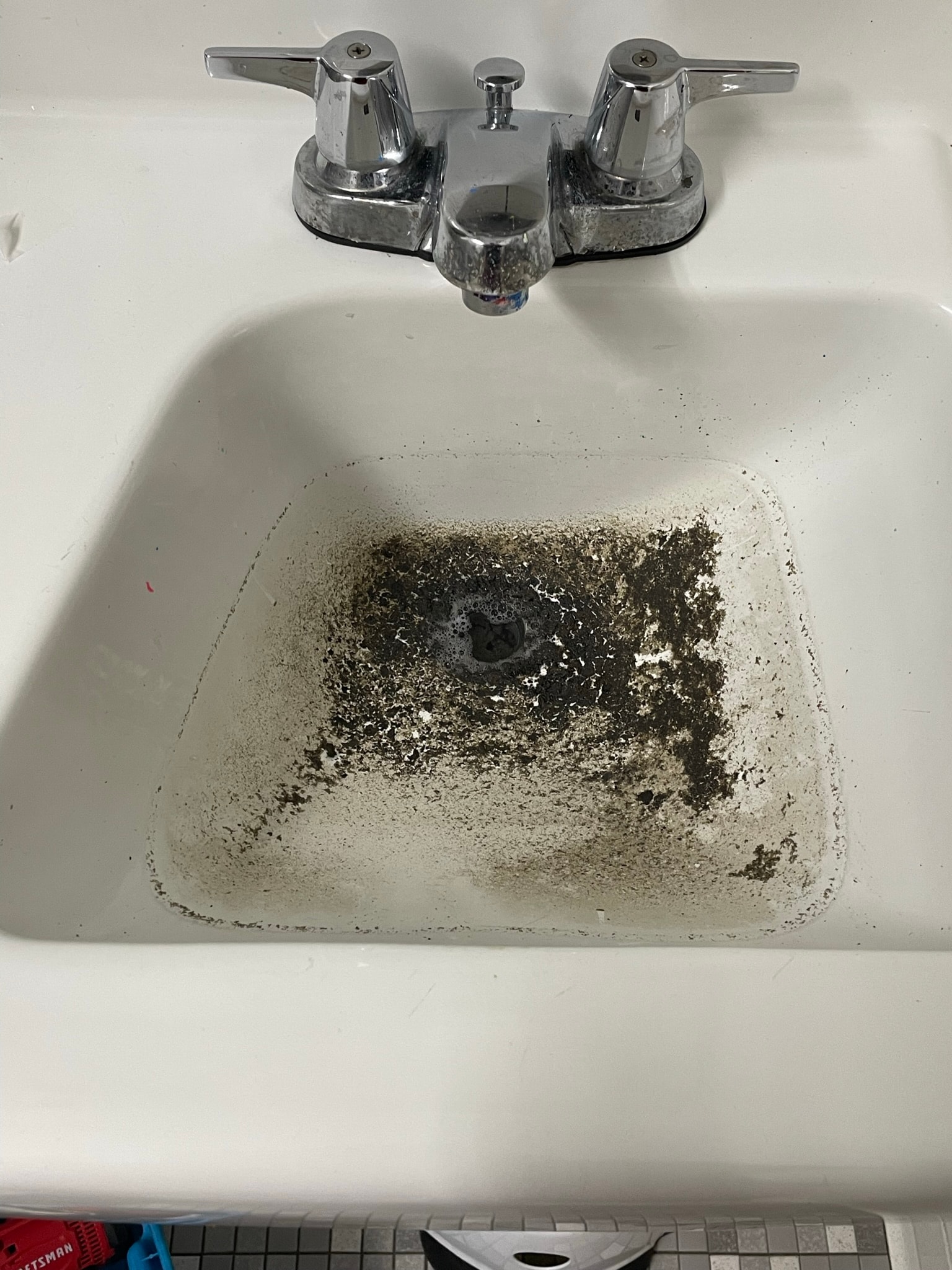 Bathroom sink before repair — heavily clogged and filthy drain basin