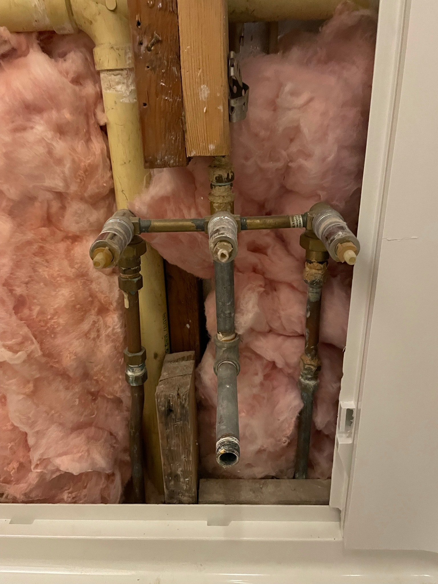 Plumbing before repair — old corroded galvanized pipes and fittings exposed in wall cavity