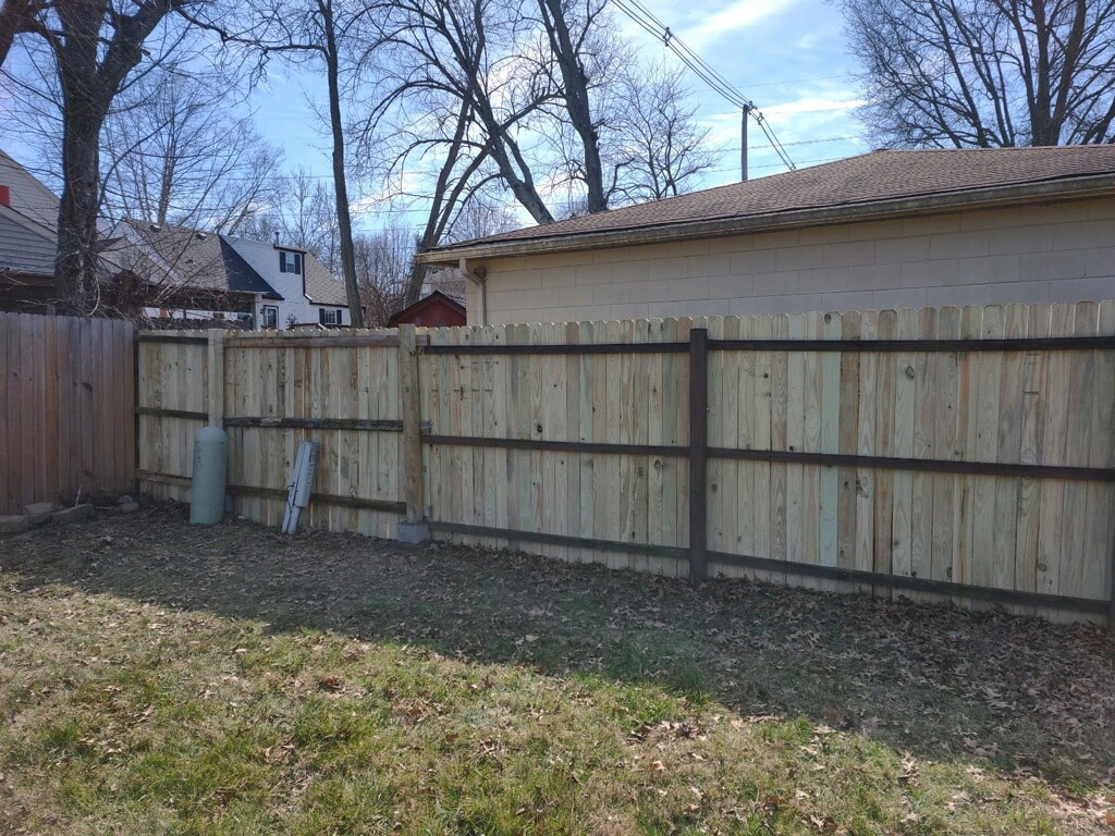 Backyard fence after replacement — brand new pressure-treated wood fence panels with dark steel posts