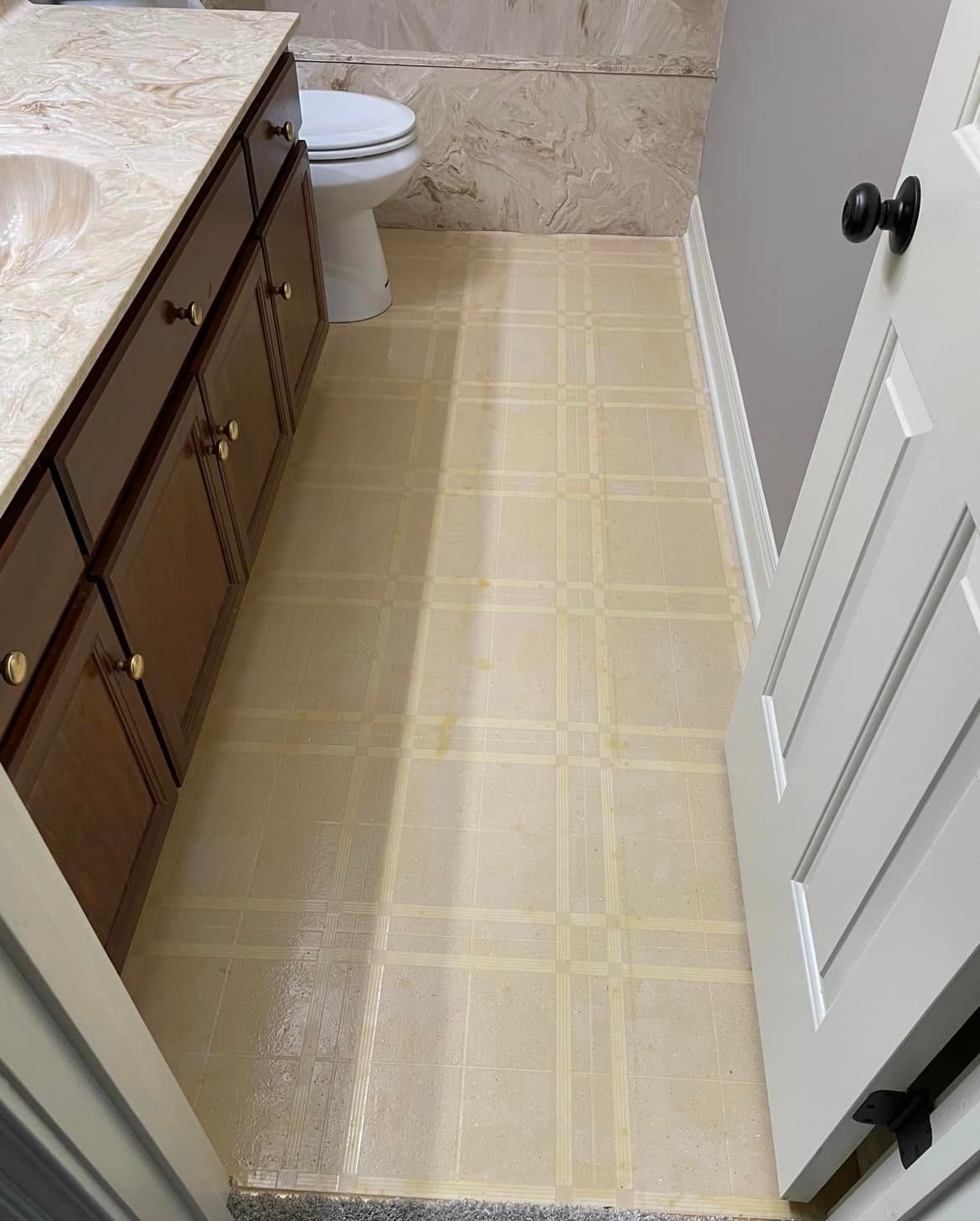 Bathroom floor before renovation — old yellowed square tile flooring showing wear and discoloration