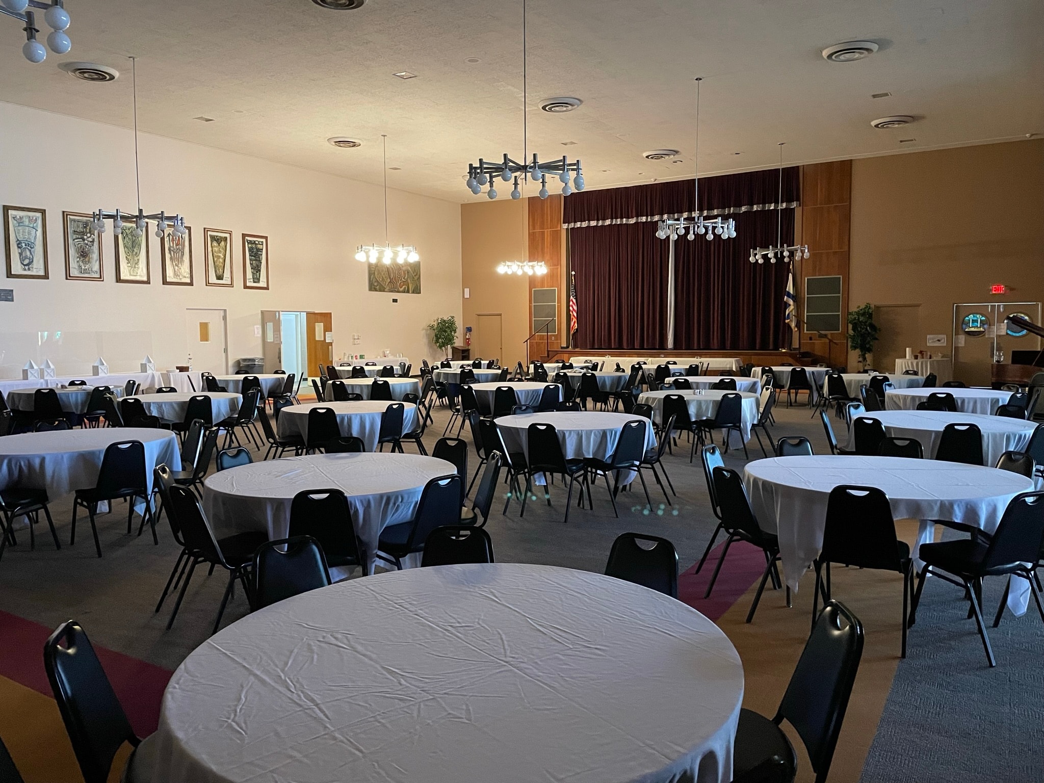 Event hall after cleaning and setup — bright banquet room with round tables, white linens, and stage ready for an event