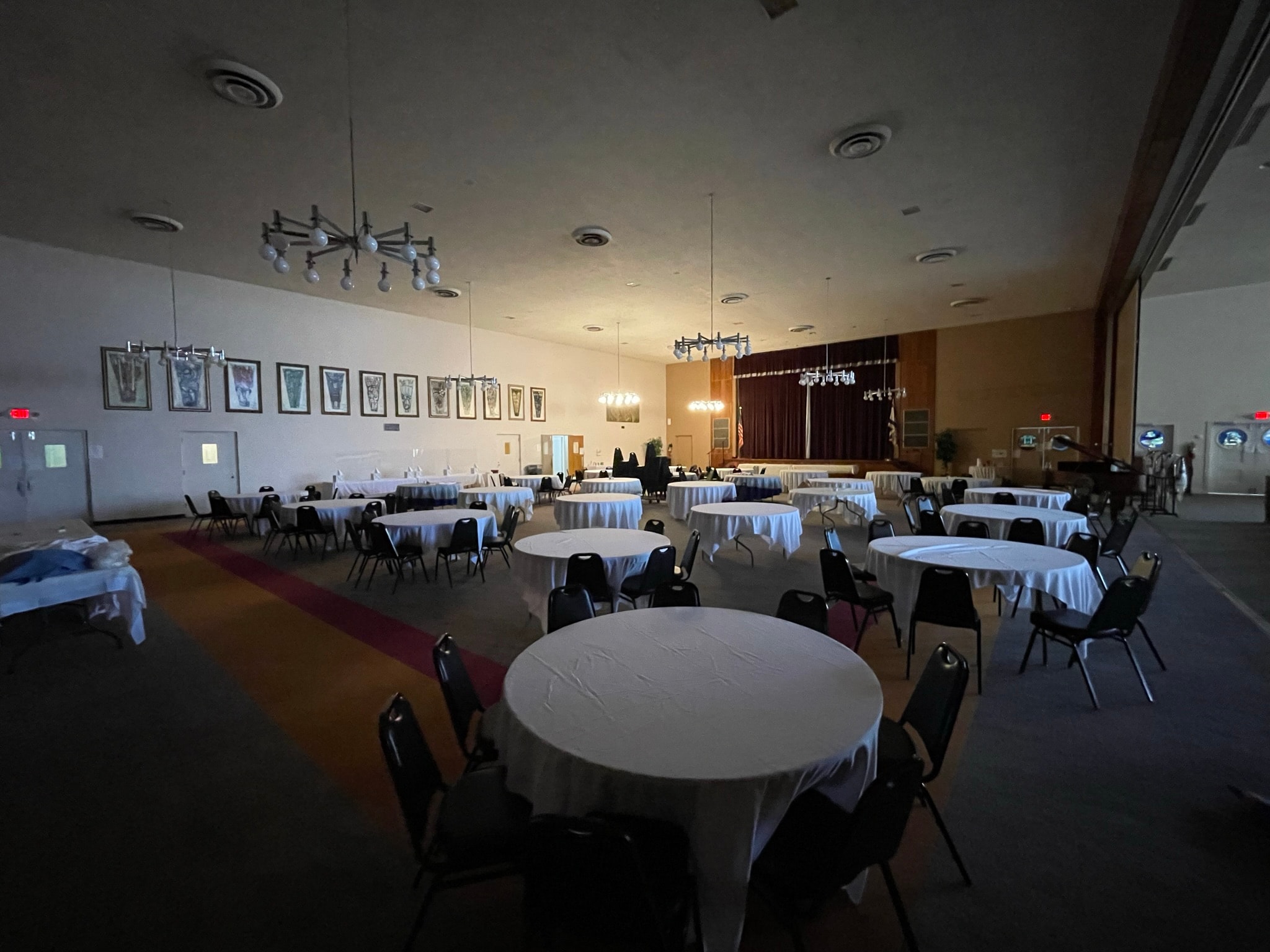 Event hall before cleaning — dim banquet room with dim lighting, scattered items, and unorganized setup