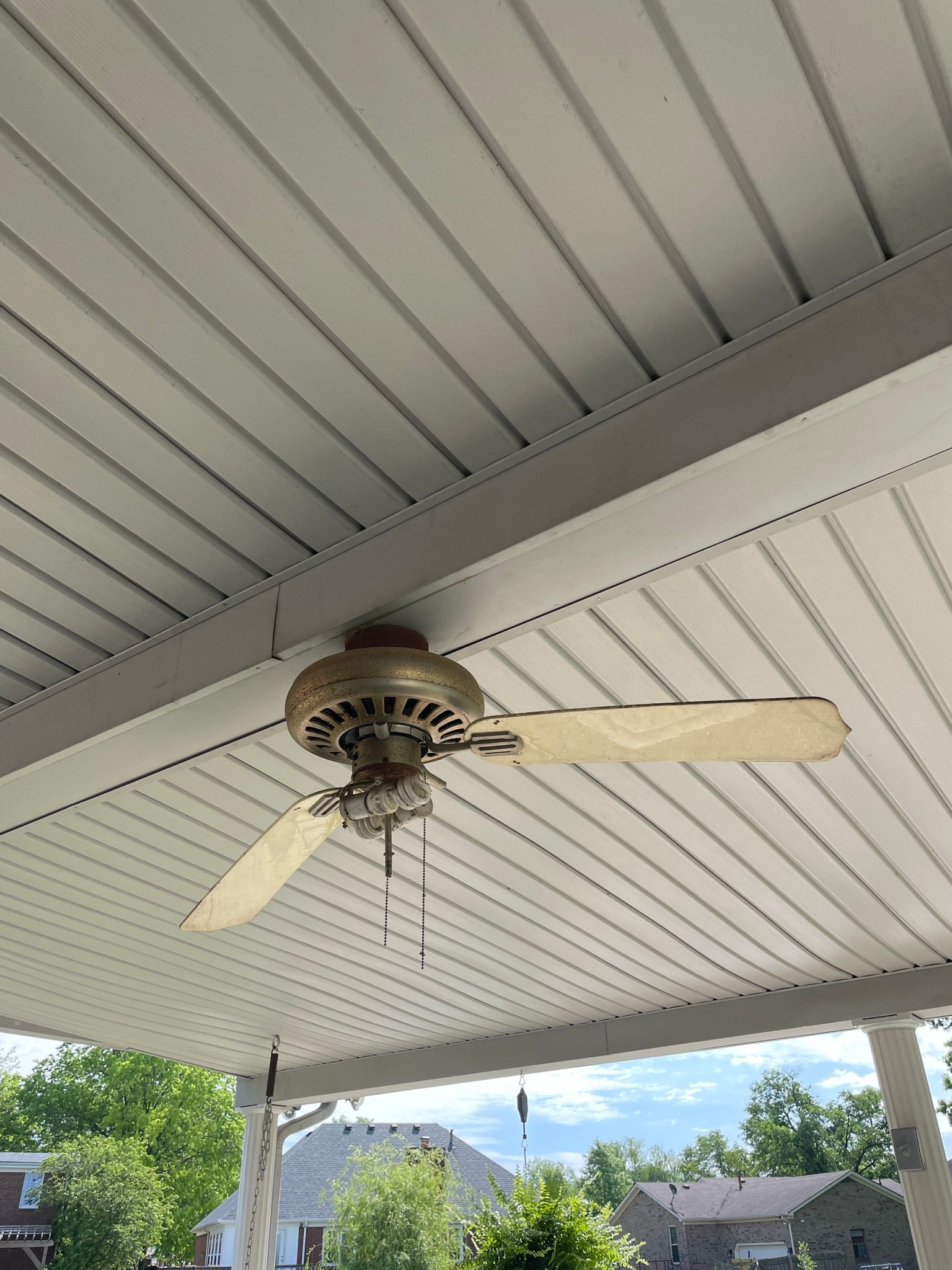 Patio ceiling before fan replacement — old rusty 3-blade ceiling fan with yellowed blades and worn motor housing