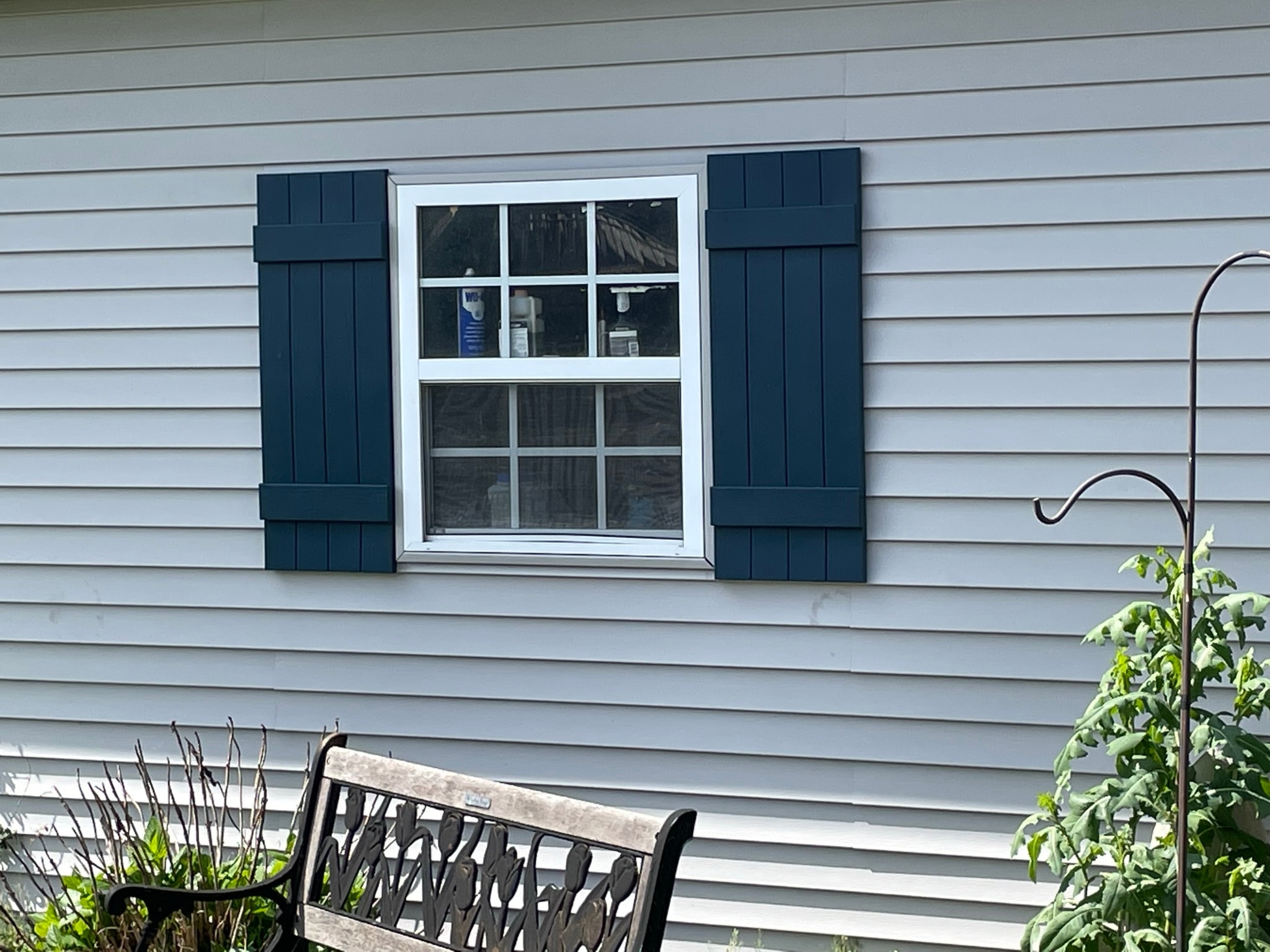 House exterior after shutter installation — same window now framed by bold navy blue board-and-batten shutters on gray siding