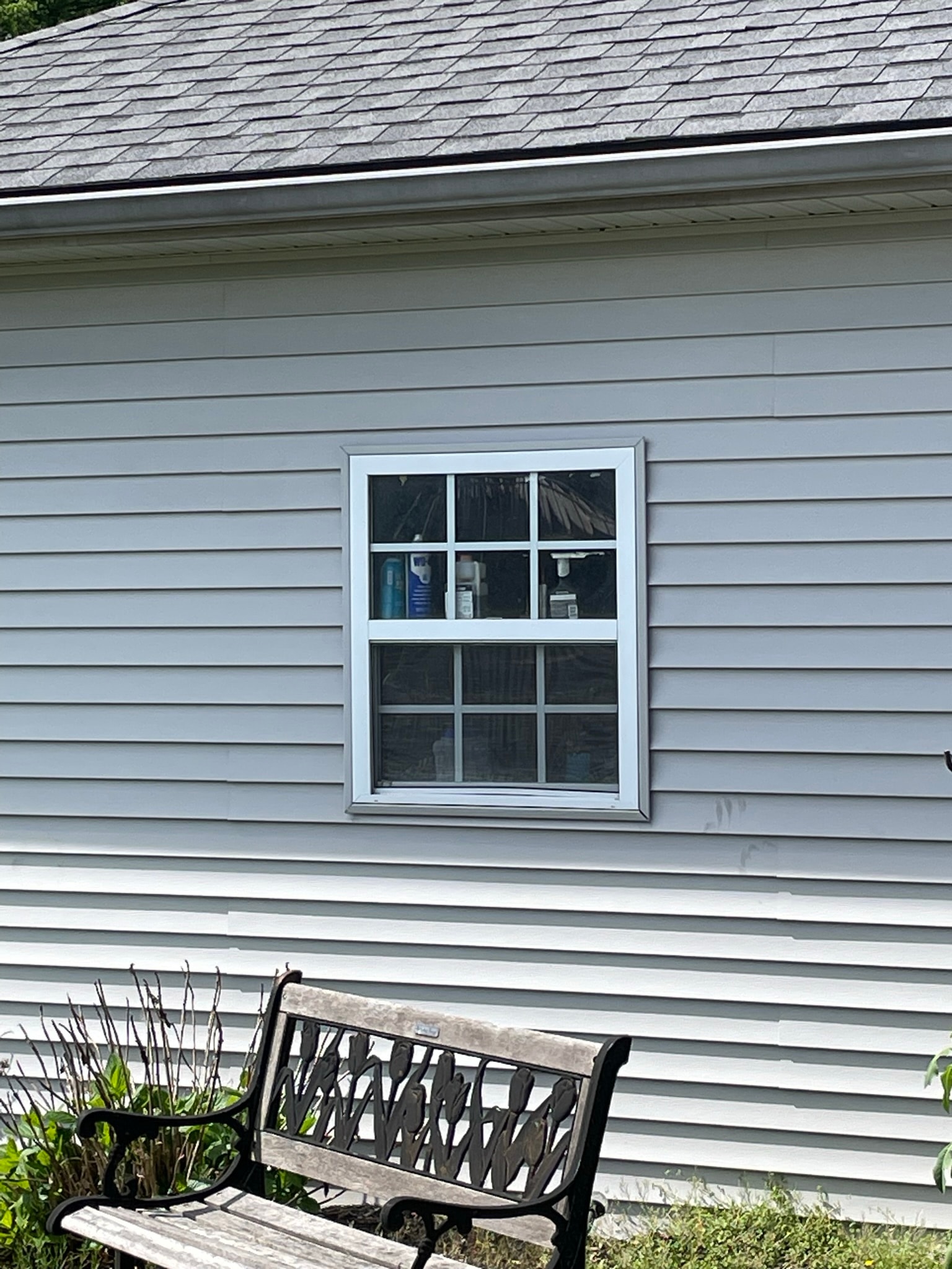 House exterior before shutter installation — plain white-trimmed window on gray vinyl siding with no shutters