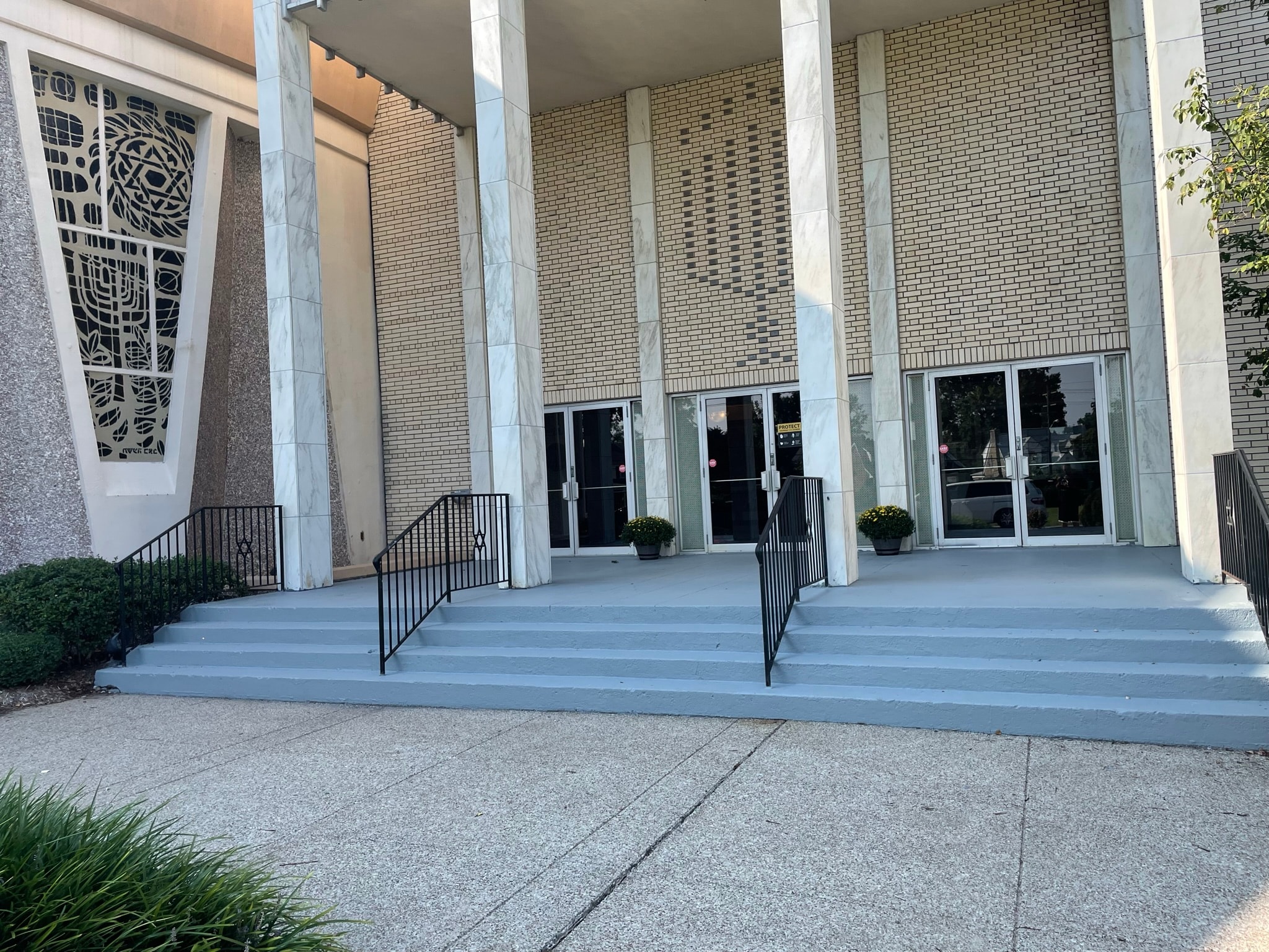 Commercial building entrance after staircase restoration — freshly painted clean grey concrete steps with potted mums flanking the doors