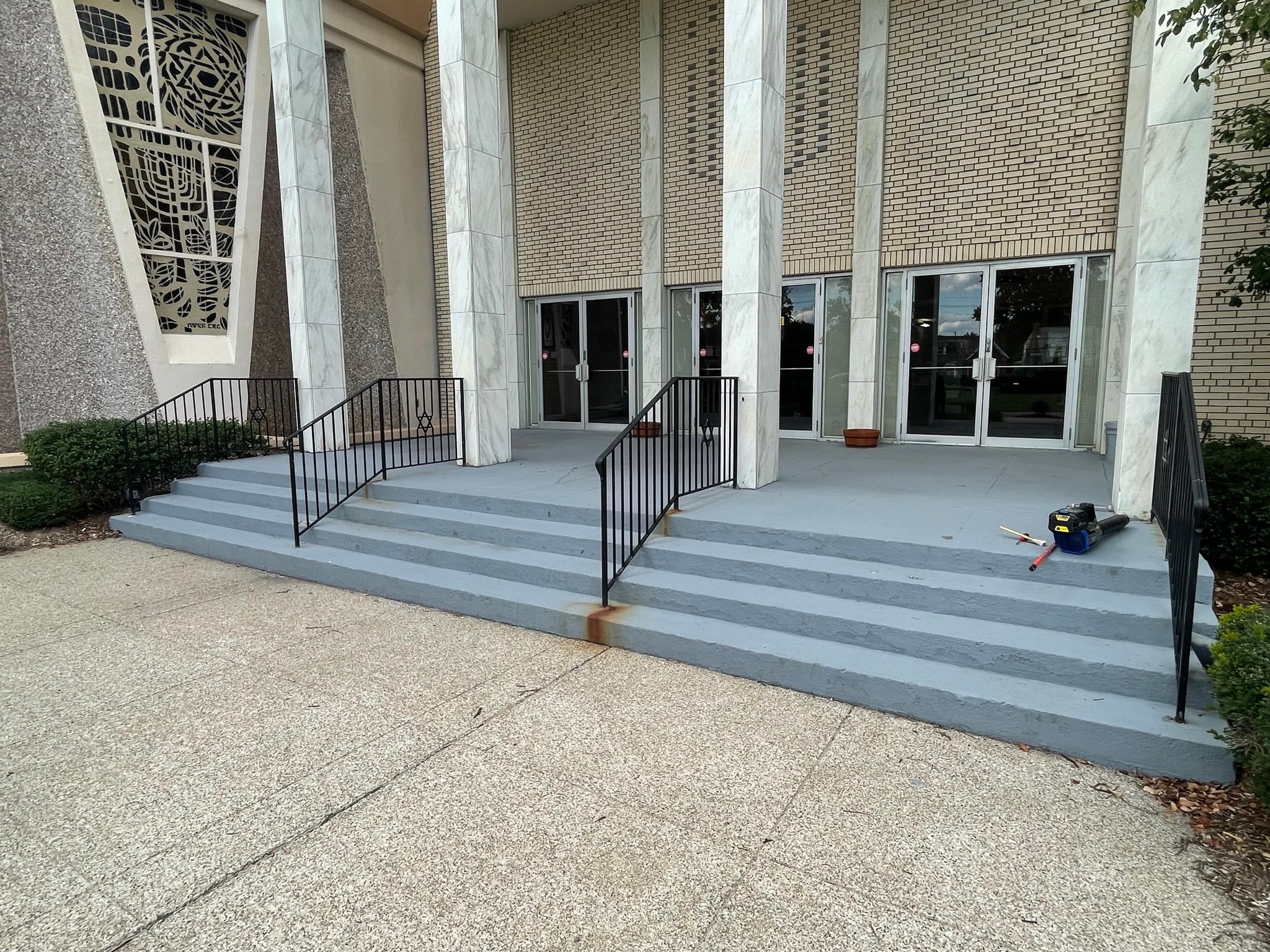 Commercial building entrance before staircase restoration — rust-stained concrete steps with tools and debris scattered on landing