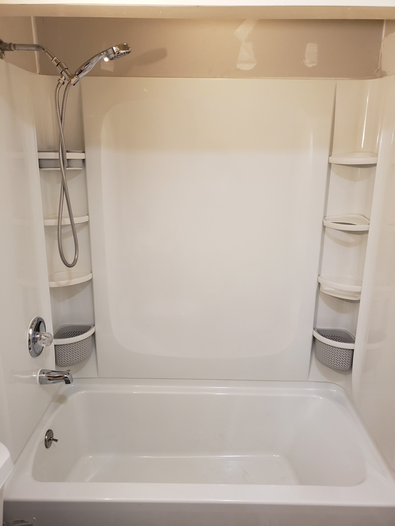 Bathroom after tub surround replacement — bright white three-piece shower surround with built-in corner shelving and modern fixtures