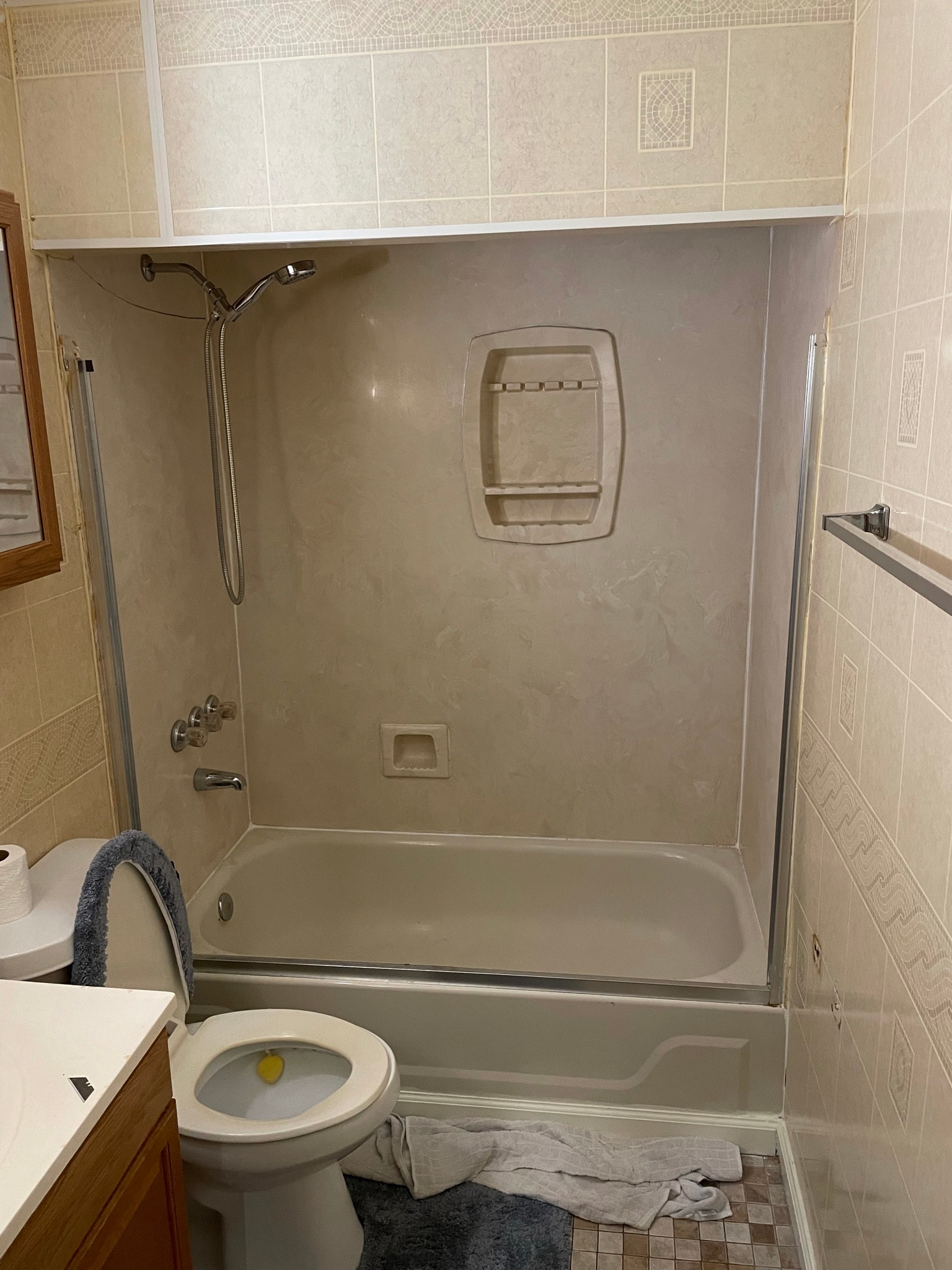 Bathroom before tub surround replacement — dingy beige one-piece shower surround with worn soap caddy and dated tile walls