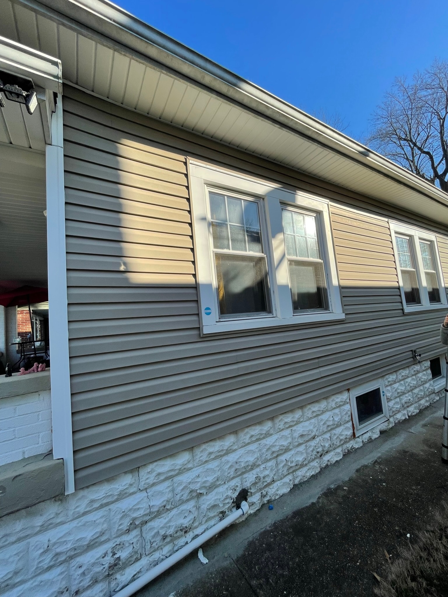 House exterior after repair — corner trim and downspout cleanly reinstalled flush against tan vinyl siding