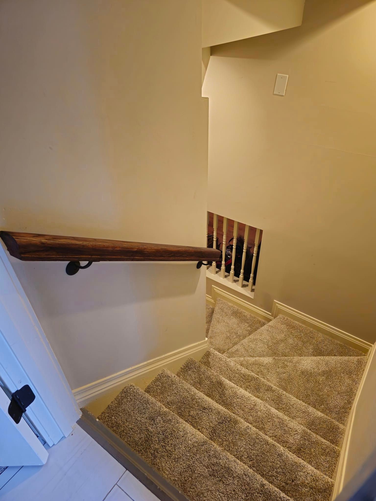 Interior staircase after handrail installation — same carpeted steps now fitted with a dark stained wood handrail mounted on black iron wall brackets