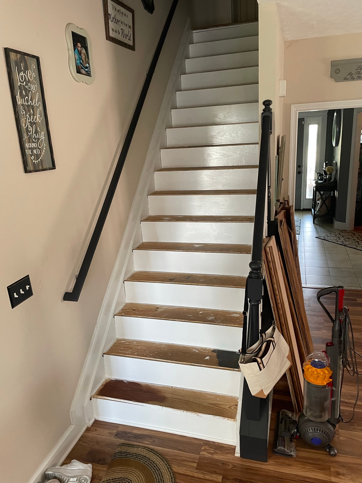 Interior staircase before tread replacement — worn mismatched wood treads mid-renovation with materials and vacuum leaning against the newel post