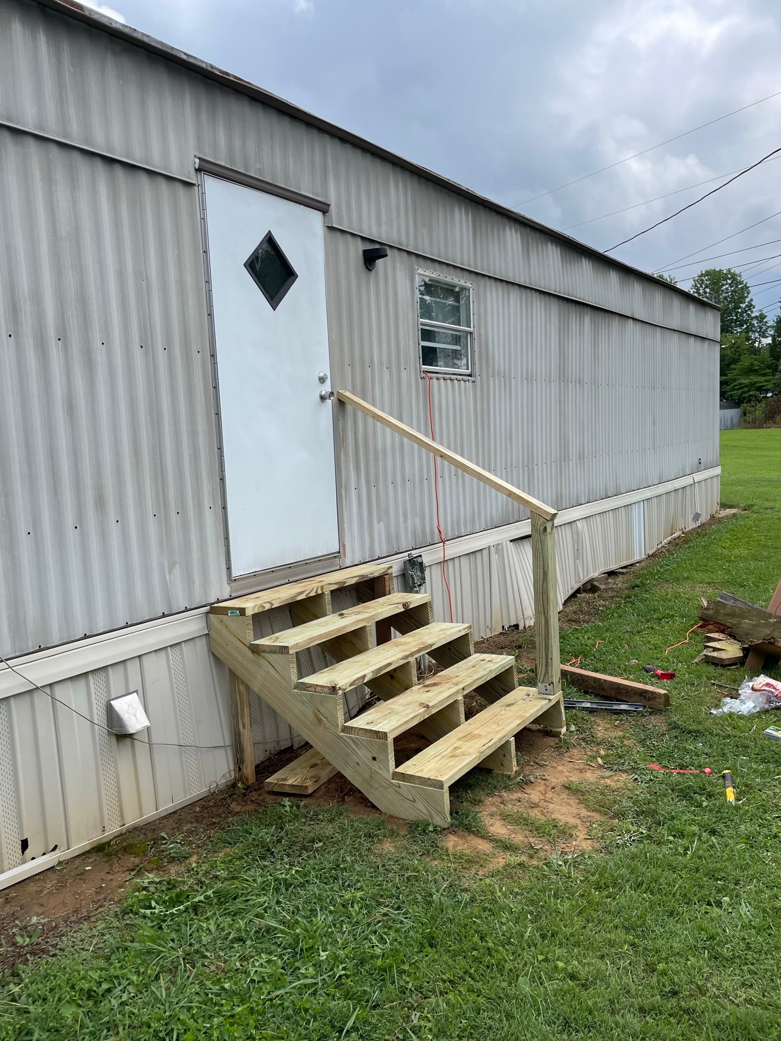 Mobile home exterior after steps replacement — brand new pressure-treated lumber entry steps with wood handrail leading to white entry door