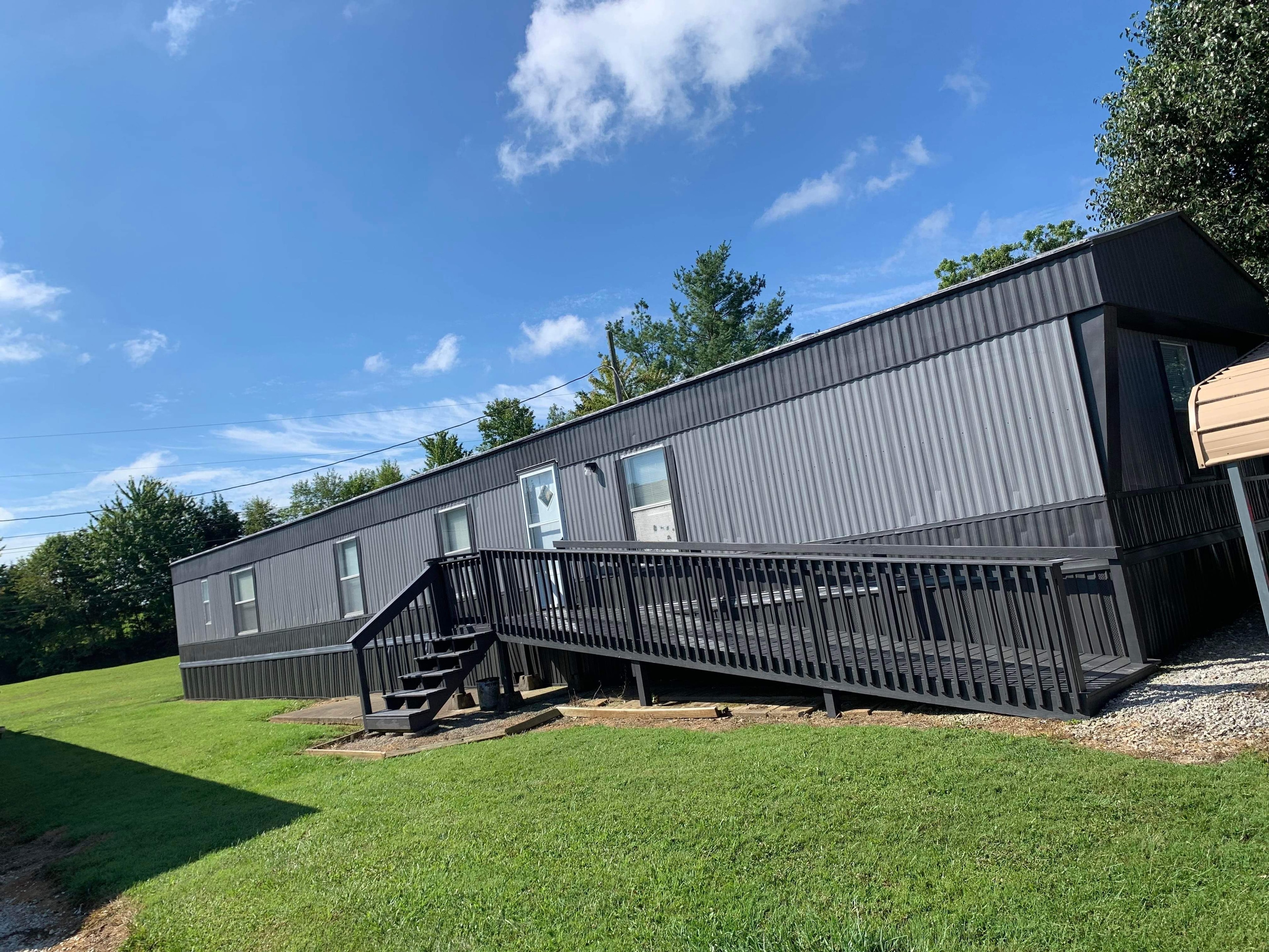 Mobile home after exterior painting — sleek black corrugated siding with matching black deck
