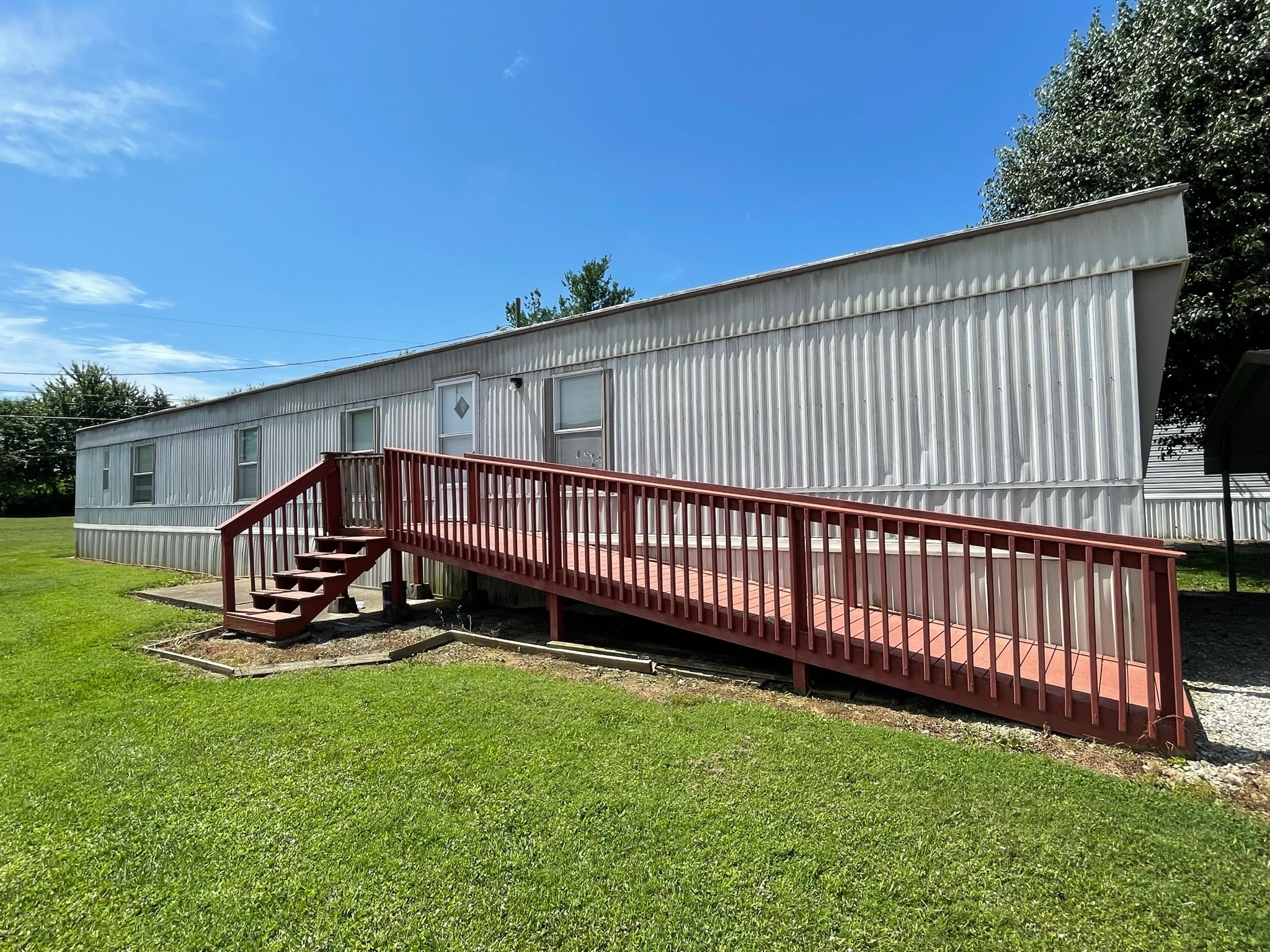 Mobile home before exterior painting — white corrugated siding with red deck