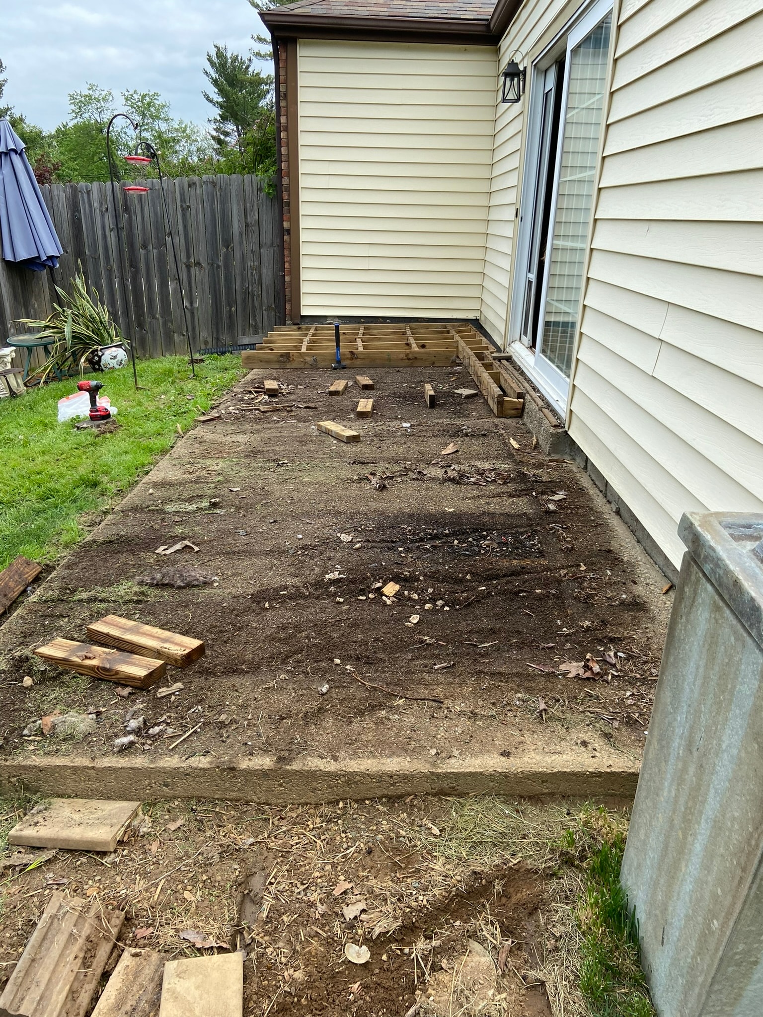 Backyard before deck build — bare concrete slab with pressure-treated framing mid-construction, scrap lumber and tools scattered on the ground