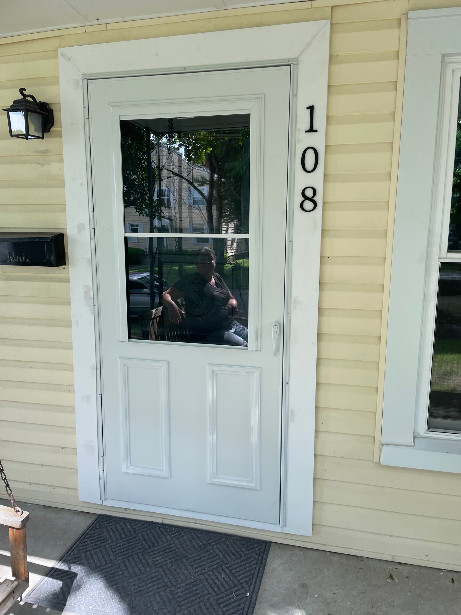 Residential front entrance after door replacement — brand new white storm door with large glass panel, clean white trim, and house number 108 on yellow vinyl siding
