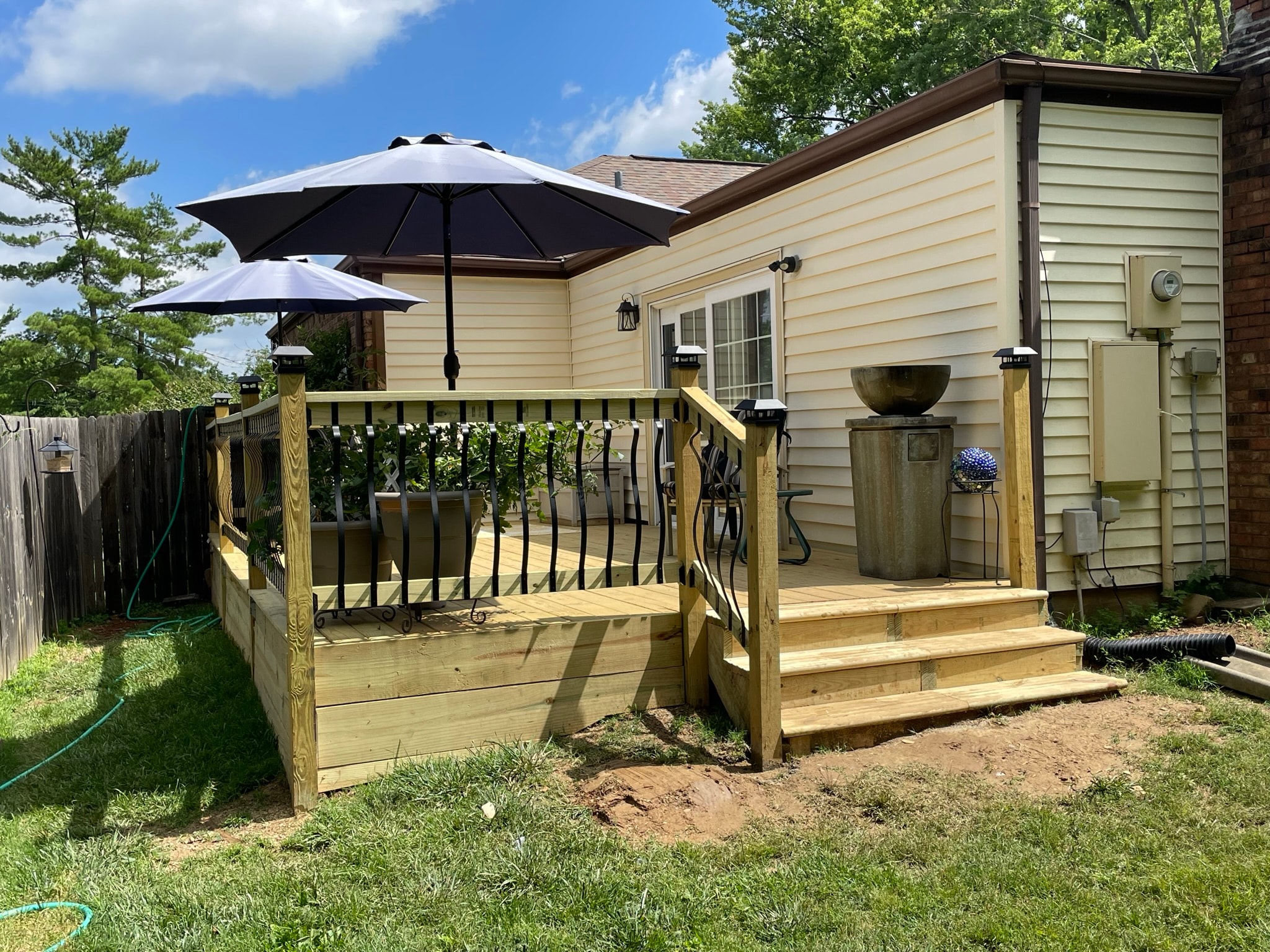 Backyard deck after renovation — brand new pressure-treated deck with decorative iron railings and solar post caps