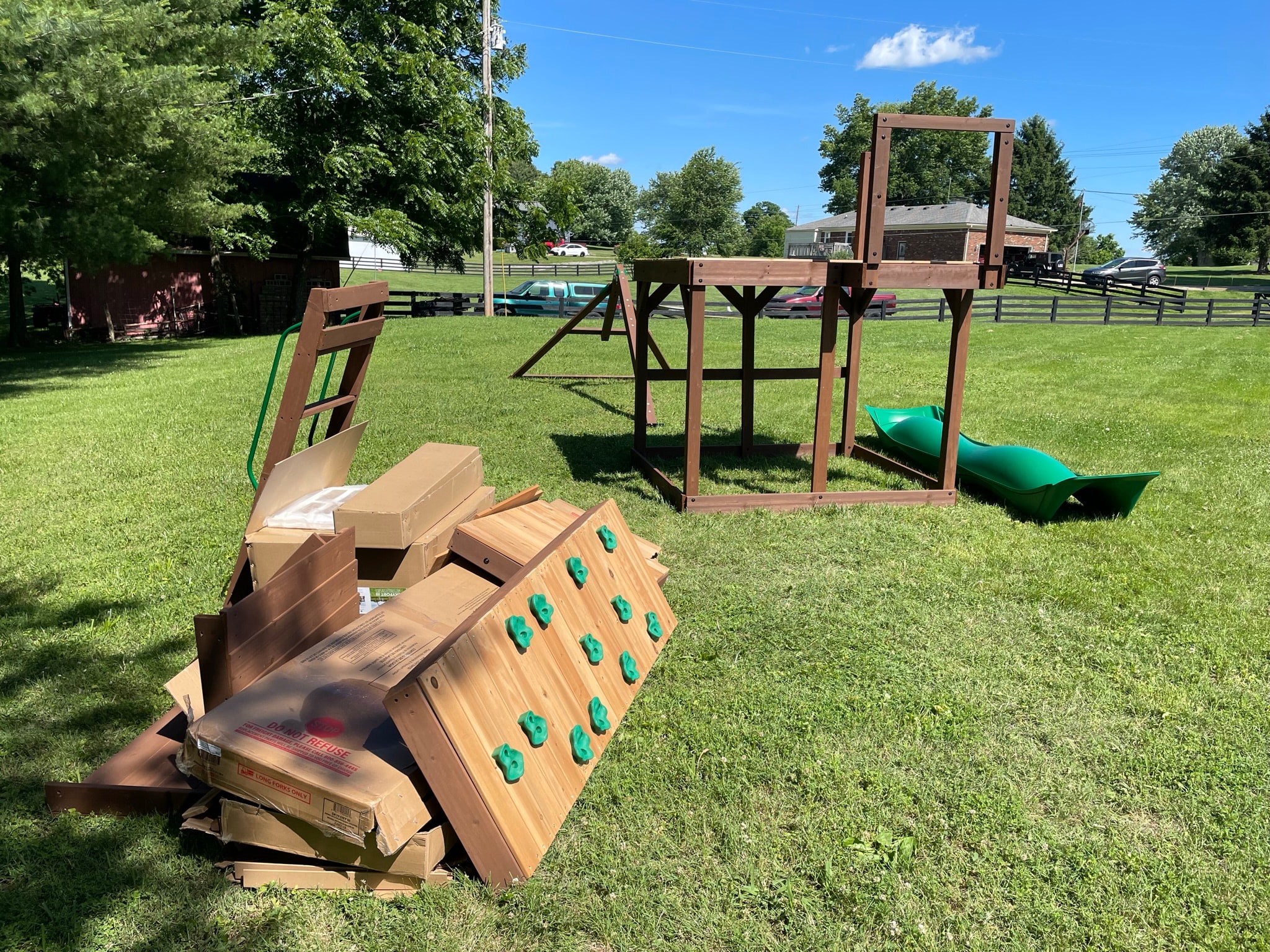 Playground set before assembly — parts, boards, and boxes scattered on grass